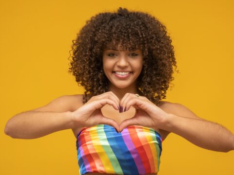 A person making a heart shape with their hands against a yellow background